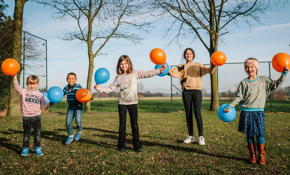 Een groepje kinderen met blauwe en oranje ballons op een grasveld