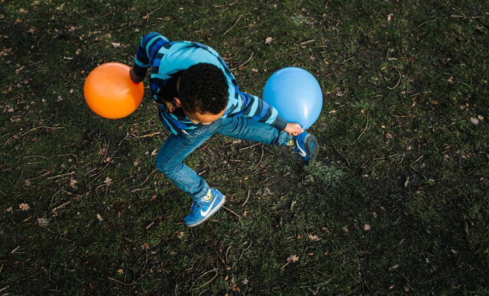 Kind met oranje en blauwe ballon op grasveld van bovenuit gezien