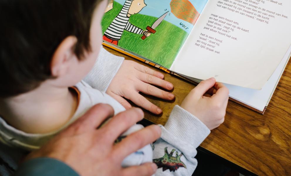 Kind oefent lezen, leerkracht legt hand op schouder