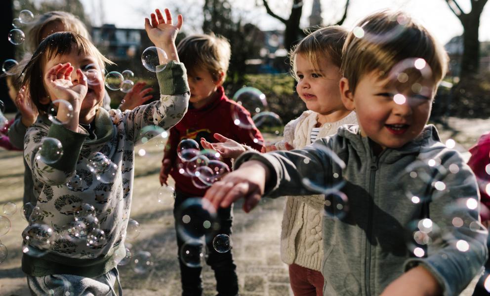 Kinderen met zeepsopbellen van bellenblaas op de kleuterspeelplaats
