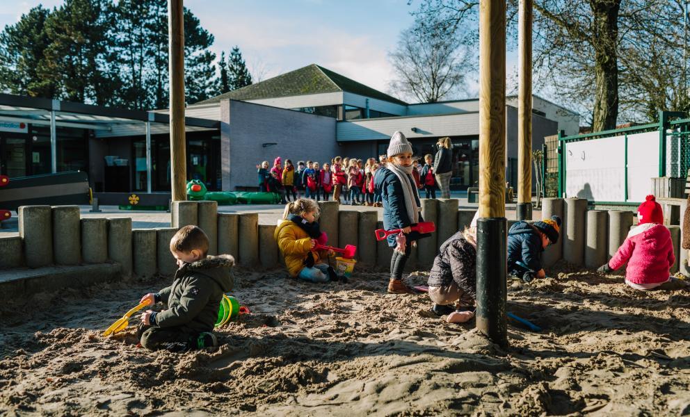 Kinderen in de zandbak met rij en leerkracht in de achtergrond