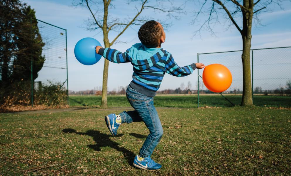 Kind springt in de lucht met blauwe en oranje ballon